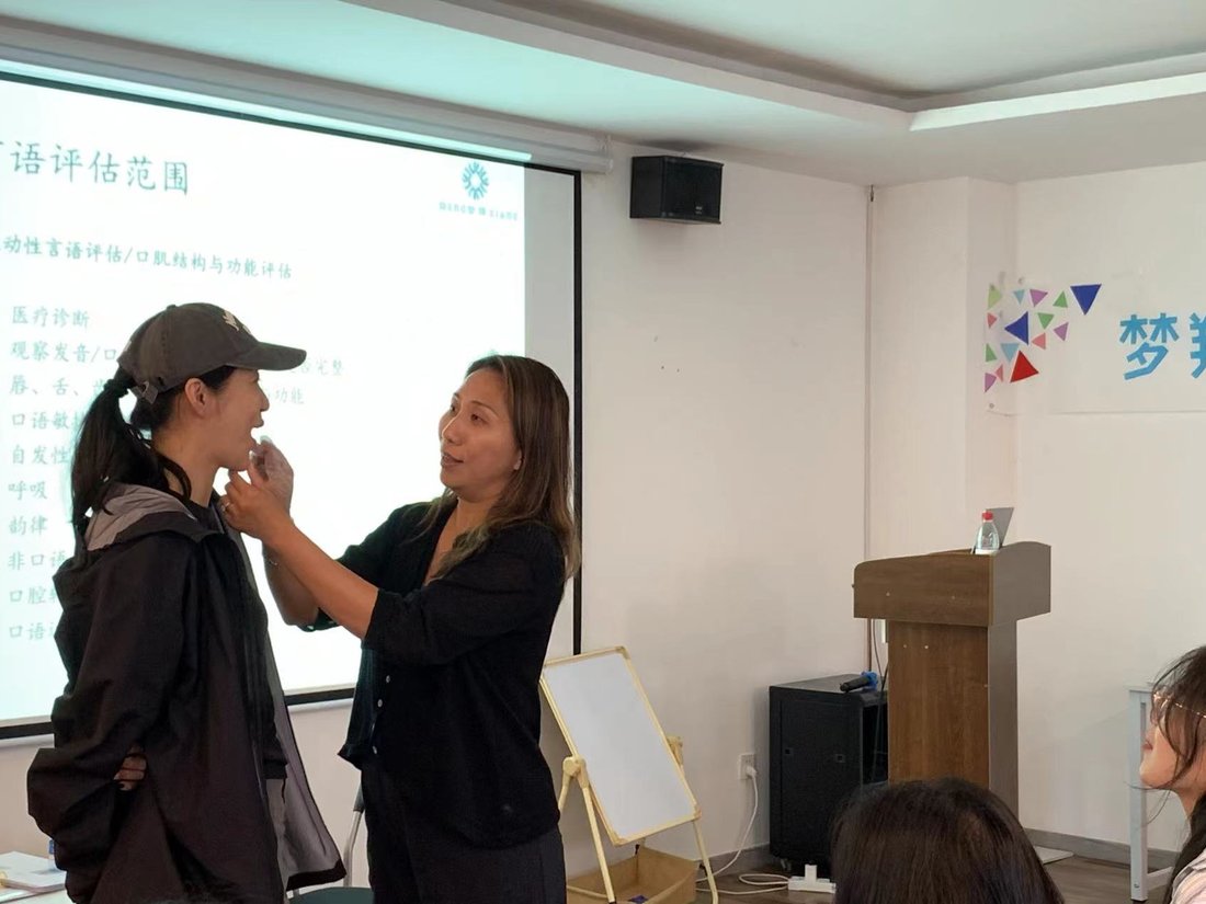 Linda Chow demonstrating an oral structure and function assessment on a workshop participant, with an assessment slide on the screen behind them